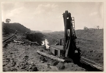 Ansicht von Arbeitern, die den Panamakanal graben, mit Eisenbahnschienen durch einen Graben und einer Art Grabmaschine im Vordergrund, 1912 oder 1913